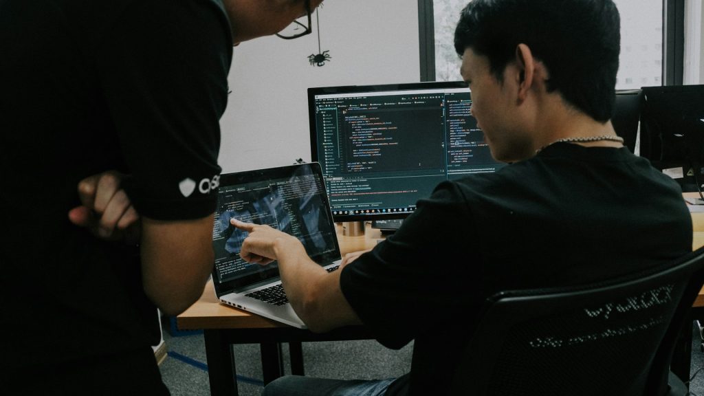 Two security analysts reviewing code on a laptop and monitor