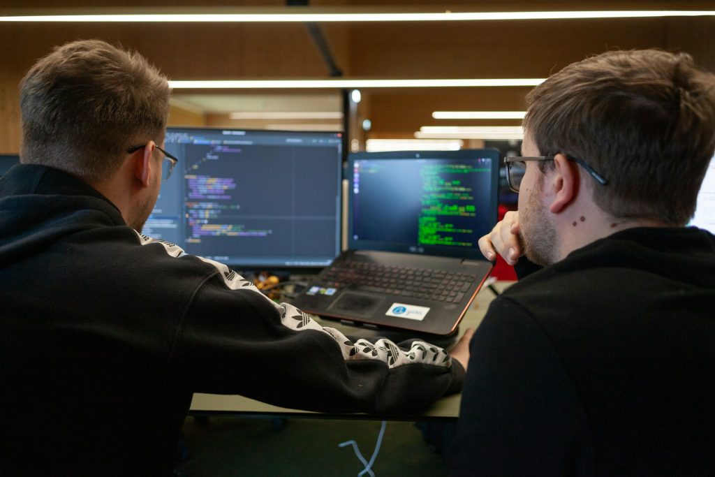 Two analysts studying code across a monitor and laptop